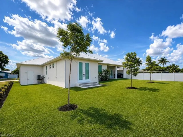 Expansive backyard featuring a manicured lawn, established trees, a white vinyl privacy fence, and a covered patio area