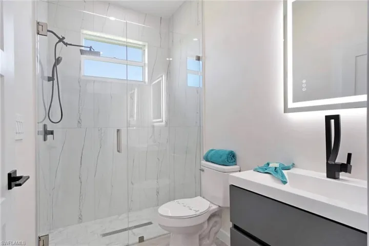 Bathroom featuring a frameless glass shower enclosure, large format white tile with gray veining, black shower fixtures, a floating vanity with a rectangular basin, and a backlit mirror