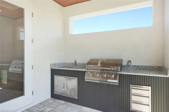 Outdoor kitchen featuring a built-in stainless steel grill, integrated sink, and stone-finish countertops