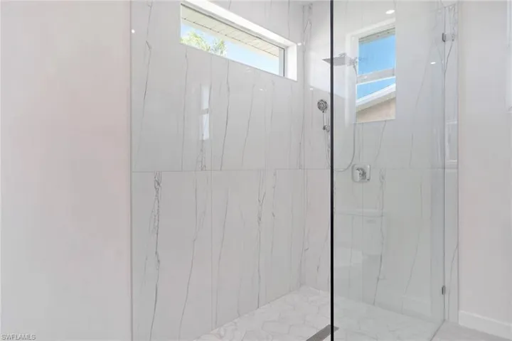 Walk-in shower featuring full-height white marble-look wall tiling, a rainfall showerhead, and a fixed glass enclosure