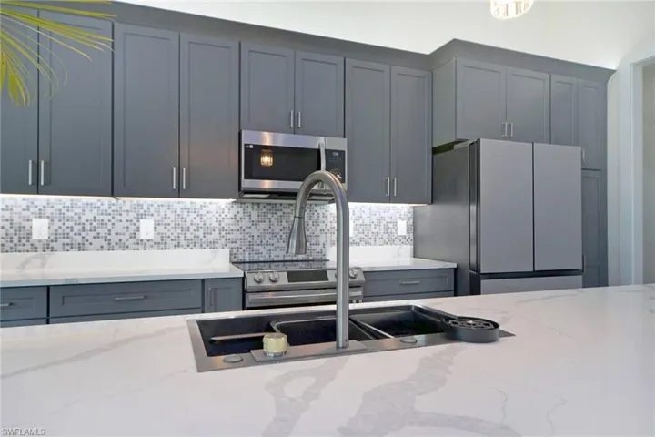 Spacious kitchen featuring an undermount sink with a gooseneck faucet, light-toned countertops, and a mosaic tile backsplash