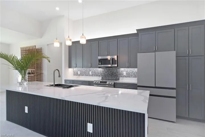 Modern kitchen featuring a large island with a white countertop and fluted paneling, gray cabinetry, stainless steel appliances, and pendant lighting