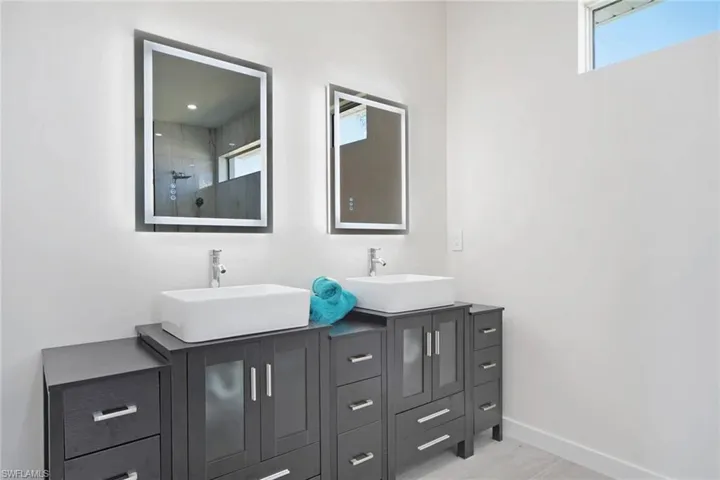 Dual vessel sinks set atop dark wood-finish vanity cabinetry with brushed nickel hardware