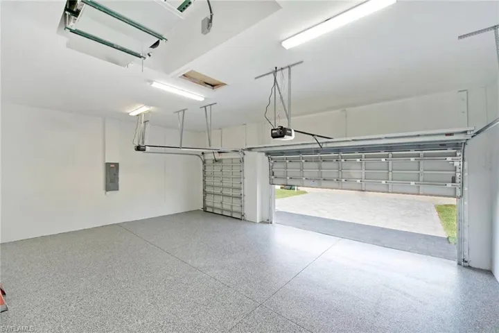 Spacious two-car garage featuring a speckled epoxy floor, white walls, and bright overhead fluorescent lighting