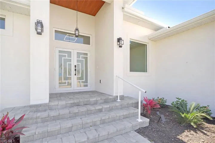 Grand entryway featuring double doors with decorative glass inserts, a transom window, and a vaulted wood-finish ceiling