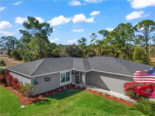 Back of property featuring a lawn, stucco siding, a shingled roof, and view of wooded area