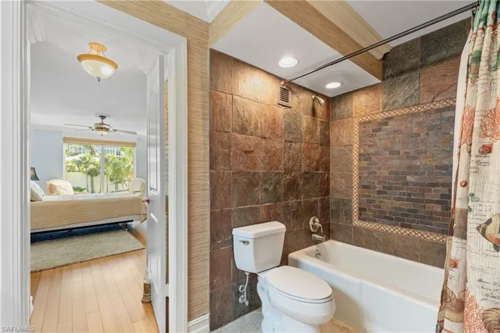 Bathroom with shower / tub combo, hardwood / wood-style floors, tile walls, ceiling fan, and toilet