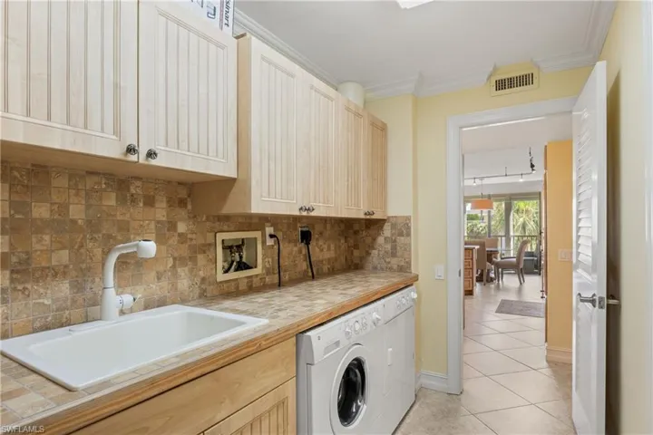 Clothes washing area featuring hookup for a washing machine, light tile flooring, sink, cabinets, and ornamental molding