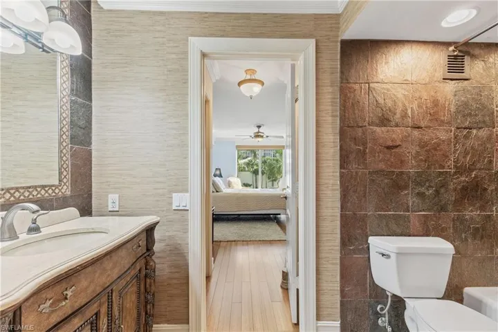 Bathroom with wood-type flooring, tile walls, ornamental molding, toilet, and vanity