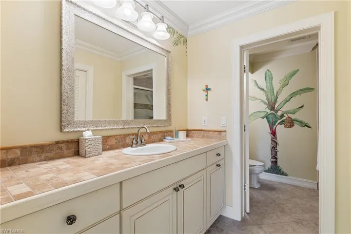 Bathroom with tile flooring, vanity with extensive cabinet space, toilet, and ornamental molding