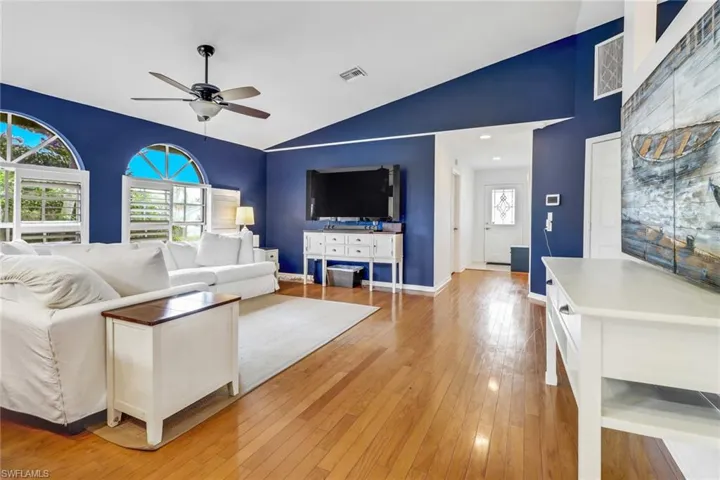 Living room with light hardwood / wood-style flooring, lofted ceiling, and ceiling fan