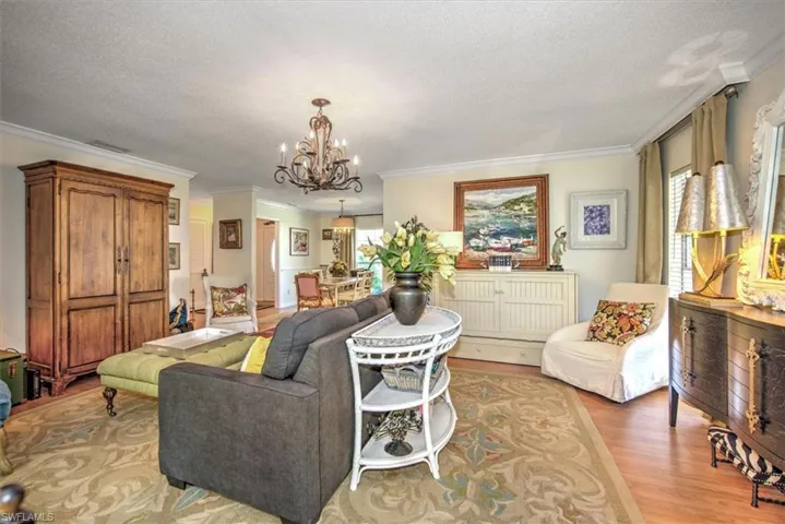 Living room with a textured ceiling, crown molding, a chandelier, and light hardwood / wood-style flooring