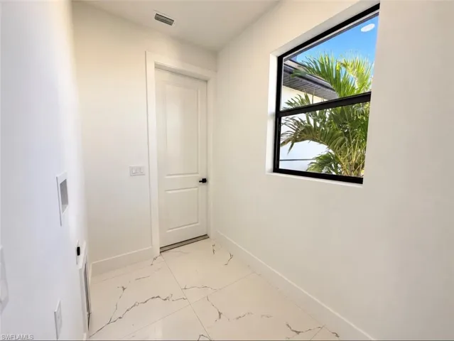 Large-format tile flooring, window with black framing, and a white paneled door with matte black hardware