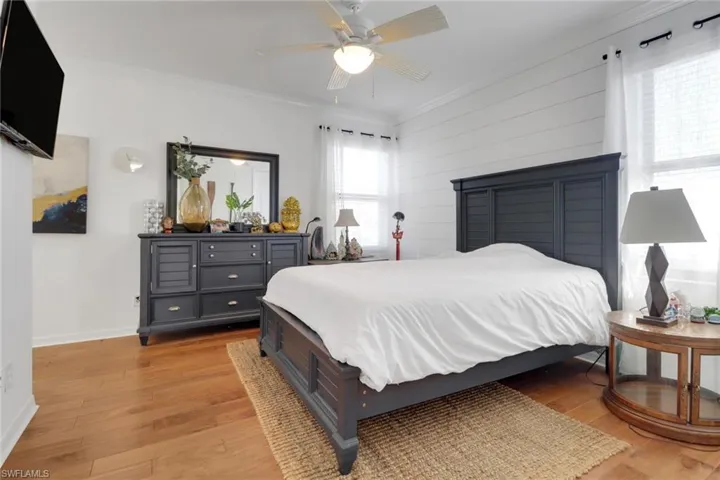 Bedroom featuring wooden walls, light hardwood / wood-style floors, ceiling fan, and crown molding