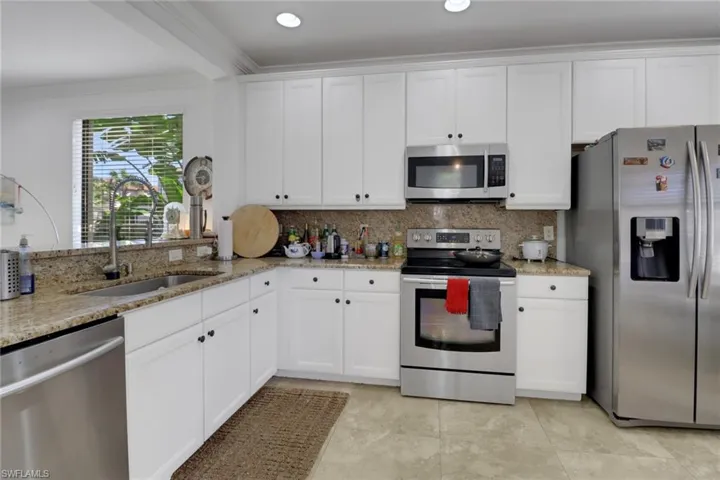 Kitchen with light stone countertops, white cabinetry, sink, and stainless steel appliances