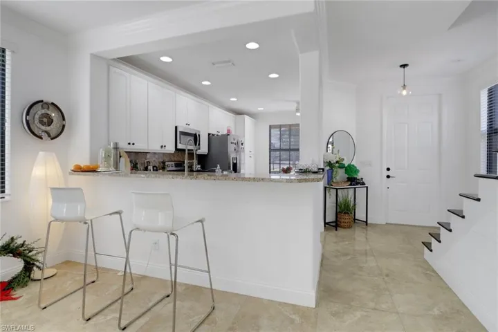 Kitchen with kitchen peninsula, backsplash, stainless steel appliances, decorative light fixtures, and white cabinets