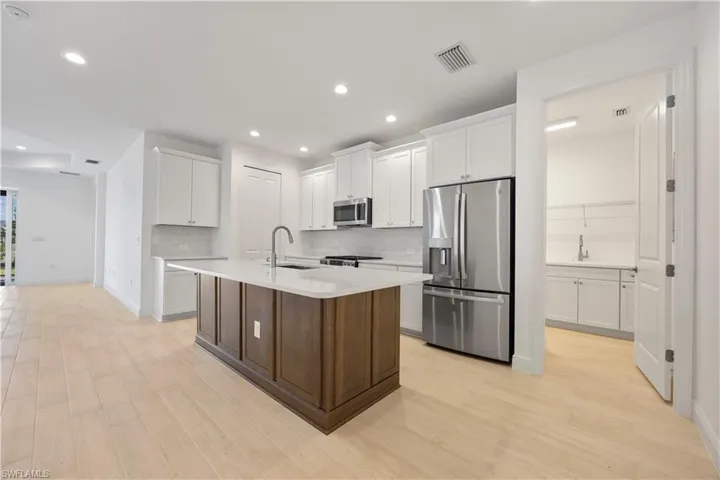 Kitchen featuring stainless steel appliances, a center island with sink, two tone cabinets, light wood finished floors, and recessed lighting