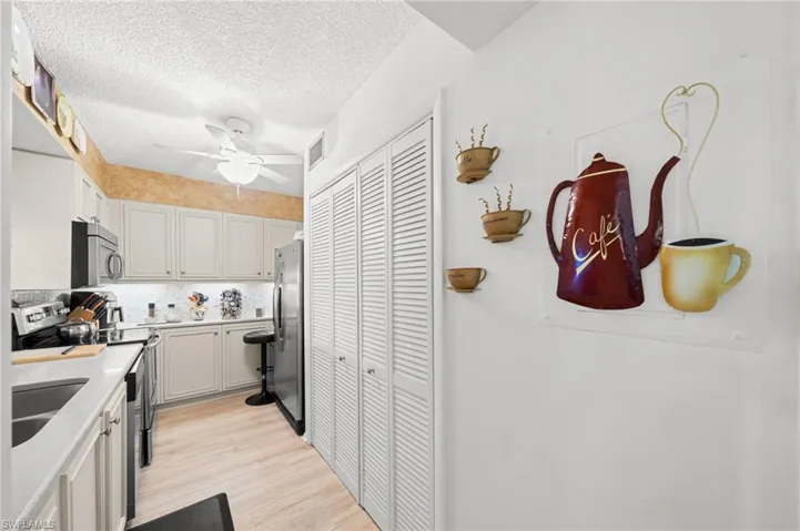 Kitchen with appliances with stainless steel finishes, tasteful backsplash, light wood-type flooring, a textured ceiling, and a ceiling fan