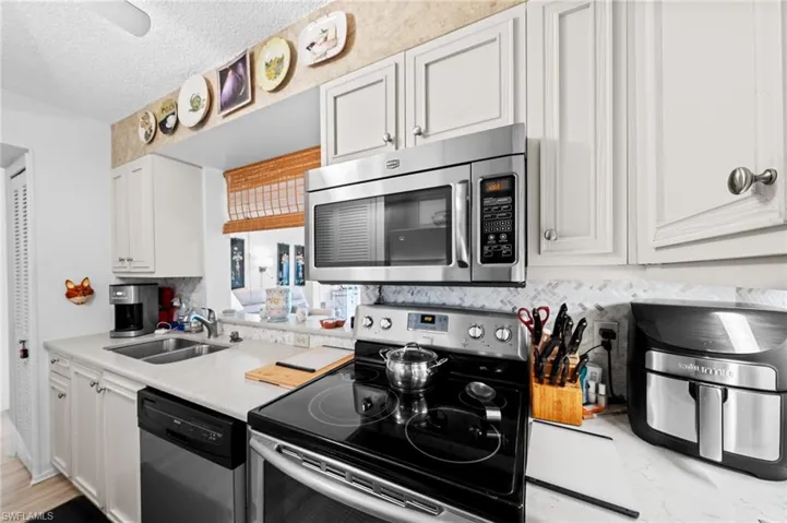 Kitchen with appliances with stainless steel finishes, a textured ceiling, white cabinetry, and backsplash
