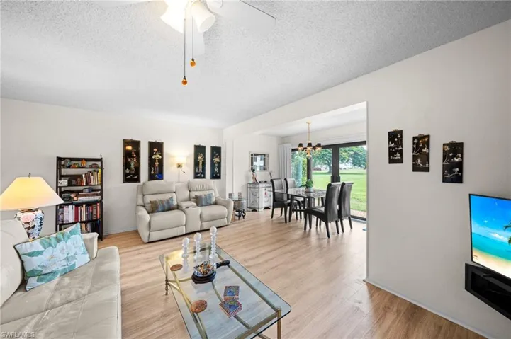 Living room featuring a textured ceiling, light wood-type flooring, a chandelier, and a ceiling fan