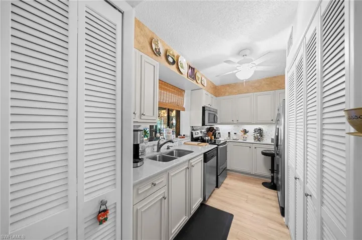 Kitchen featuring a textured ceiling, appliances with stainless steel finishes, light wood finished floors, tasteful backsplash, and light stone countertops