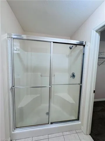Full bath featuring a shower stall, a walk in closet, a textured ceiling, and tile patterned floors