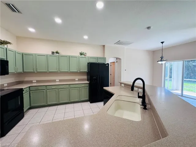 Kitchen with green cabinets, black appliances, arched walkways, hanging light fixtures, and light countertops