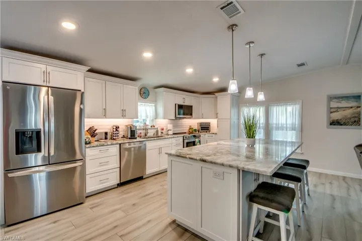 Kitchen featuring appliances with stainless steel finishes, light stone countertops, white cabinetry, decorative backsplash, and a chandelier