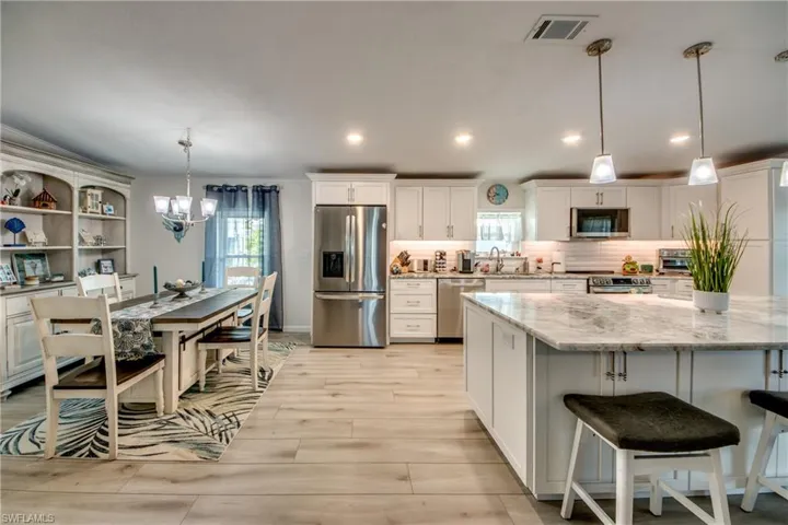 Kitchen with stainless steel appliances, white cabinets, light stone countertops, crown molding, and recessed lighting