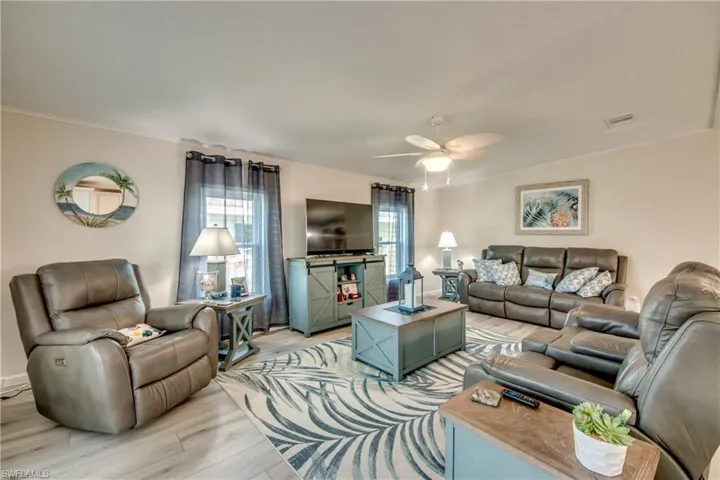 Living room featuring vaulted ceiling, a chandelier, light wood-style flooring, ceiling fan, and healthy amount of natural light