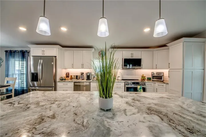 Kitchen with backsplash, appliances with stainless steel finishes, white cabinetry, light stone countertops, and recessed lighting