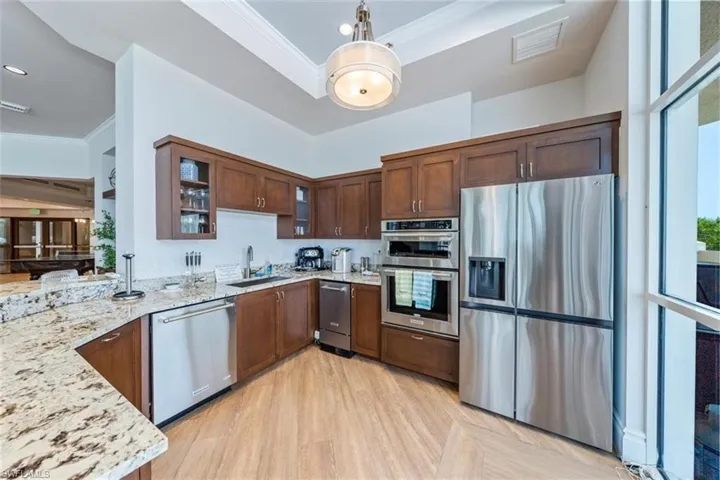 Kitchen with ornamental molding, light stone countertops, sink, and stainless steel appliances