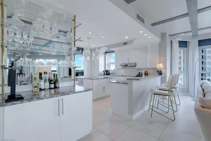 Kitchen featuring light stone counters, an island with sink, decorative light fixtures, backsplash, and white cabinetry