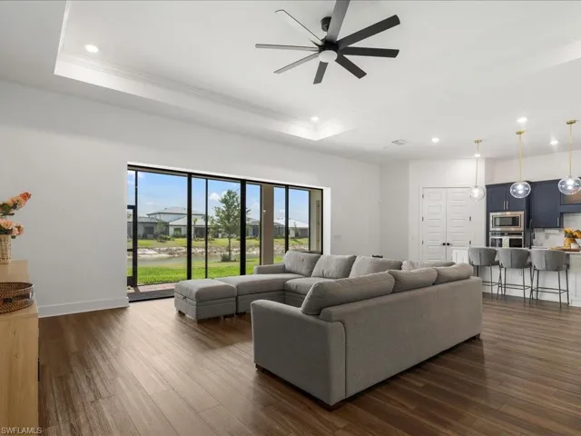 Living room featuring dark wood-style flooring, a ceiling fan, a tray ceiling, and recessed lighting