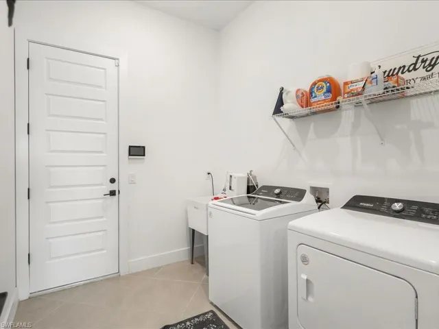 Clothes washing area featuring baseboards, washer and clothes dryer, laundry area, and light tile patterned flooring