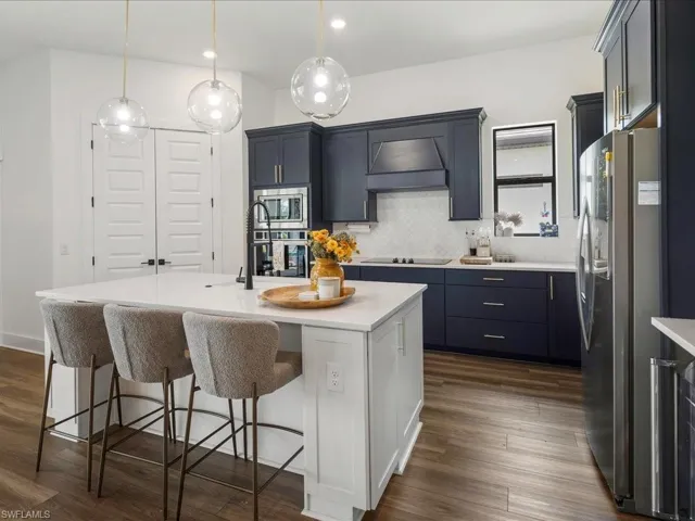 Kitchen with decorative backsplash, a breakfast bar, stainless steel appliances, light countertops, and dark wood-style floors