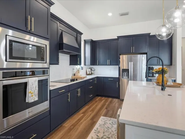 Kitchen with a sink, stainless steel appliances, custom range hood, backsplash, and visible vents