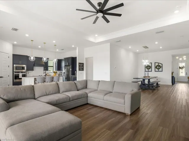 Living area featuring recessed lighting, visible vents, dark wood-style floors, and ceiling fan with notable chandelier
