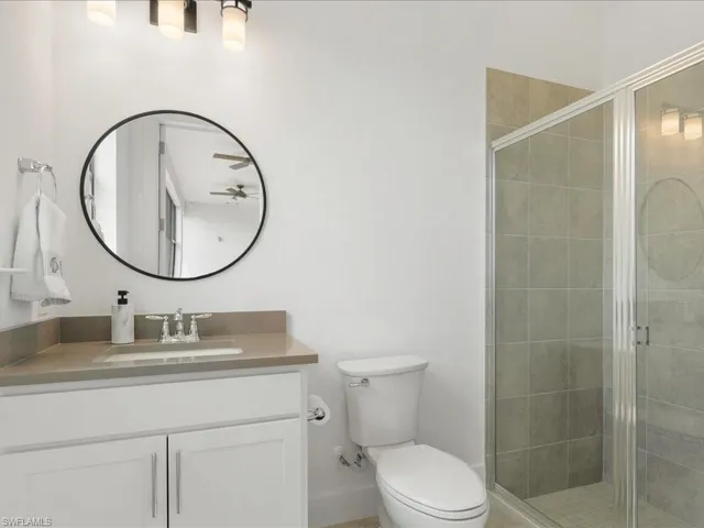 Bathroom with toilet, a ceiling fan, vanity, and a stall shower