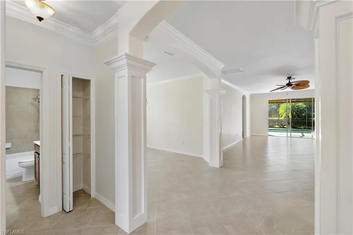 Hallway featuring crown molding, baseboards, light tile patterned floors, arched walkways, and ornate columns