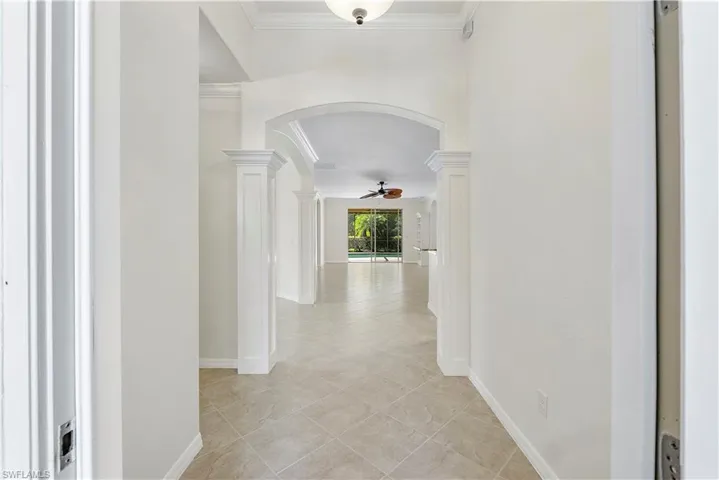 Hall featuring arched walkways, baseboards, crown molding, and ornate columns