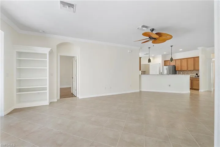 Unfurnished living room featuring crown molding, arched walkways, visible vents, and ceiling fan