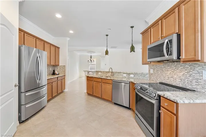 Kitchen featuring decorative light fixtures, stainless steel appliances, a peninsula, and crown molding