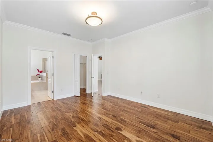 Unfurnished bedroom featuring visible vents, baseboards, wood finished floors, and ornamental molding