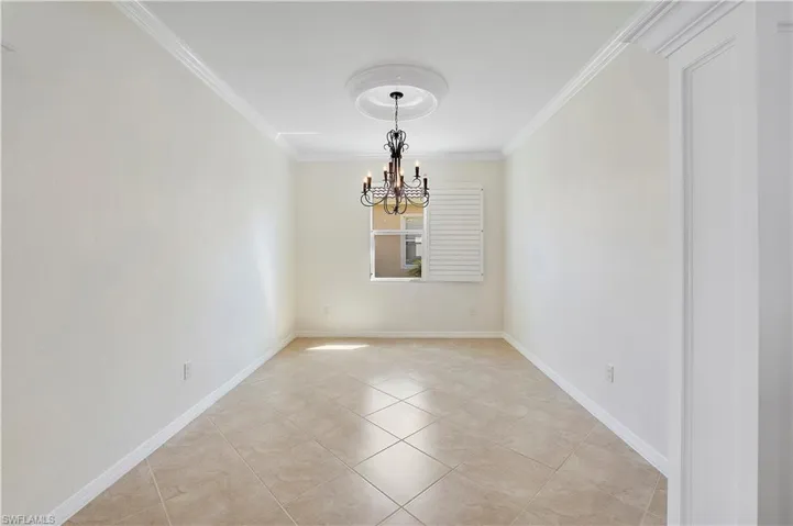Spare room with a chandelier, crown molding, baseboards, and light tile patterned flooring