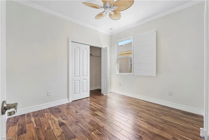 Unfurnished bedroom with wood finished floors, a closet, crown molding, baseboards, and ceiling fan