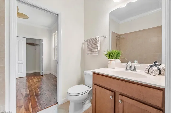 Bathroom with wood finished floors, tiled shower, toilet, and ornamental molding