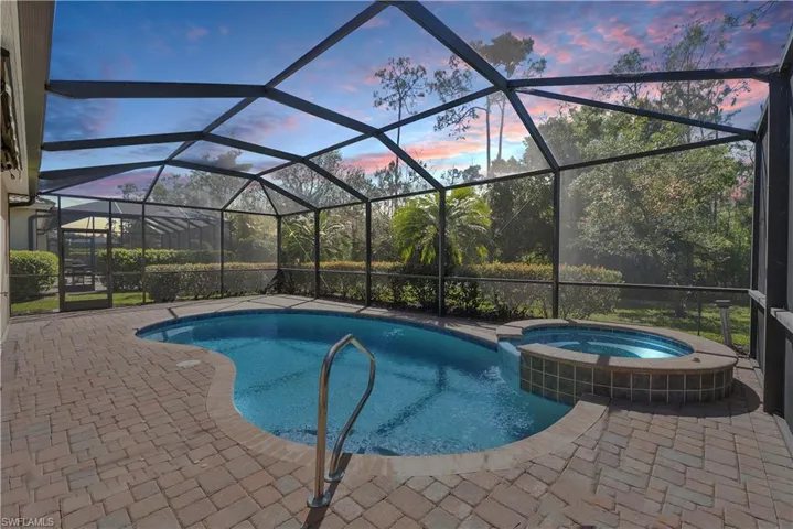 Pool at dusk featuring a patio area, enclosure, and a heated pool with connected hot tub, and private views.