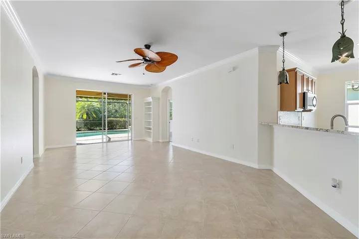Unfurnished living room with visible vents, baseboards, ceiling fan, ornamental molding, and arched walkways