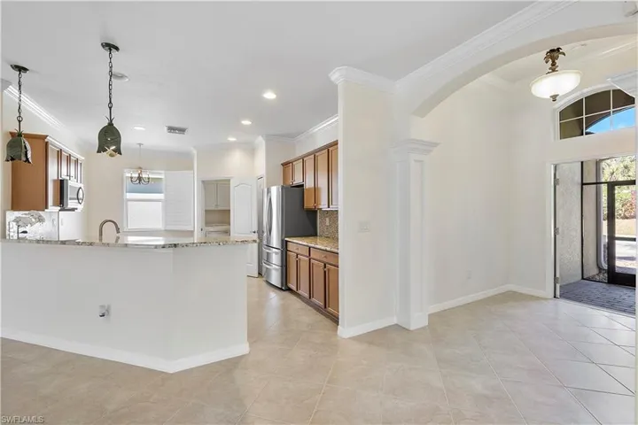 Kitchen featuring brown cabinetry, appliances with stainless steel finishes, light stone countertops, and arched walkways